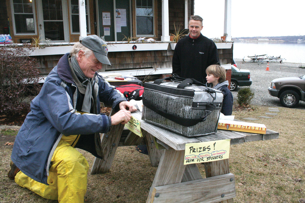 PRIZE TABLE: Bill Sawicki, one of Edgewood’s racers, and his son Will, an up and coming sailor, look over the prizes many of which were donated by members of the Marine Trades Association. Jonathan Howard arranges the display outside the house that has served as club headquarters since Edgewood burned to the water a year ago.