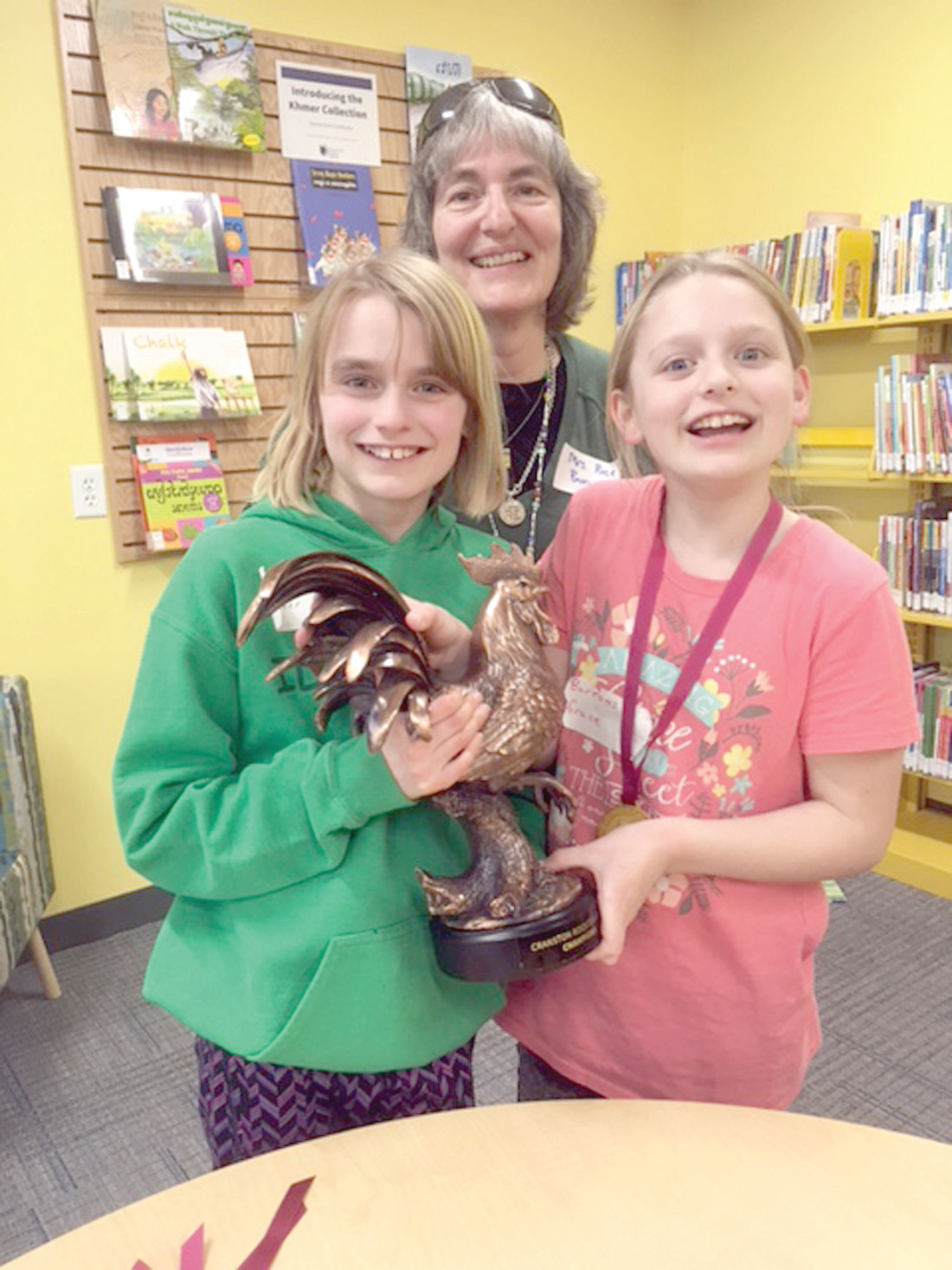 TROPHY COMES HOME TO ROOST: Getting their hands on the first Rooster Games Trophy are Barrows students Kara Bush and Grace Michaelson alongside Barrows School Librarian Sue Rose.