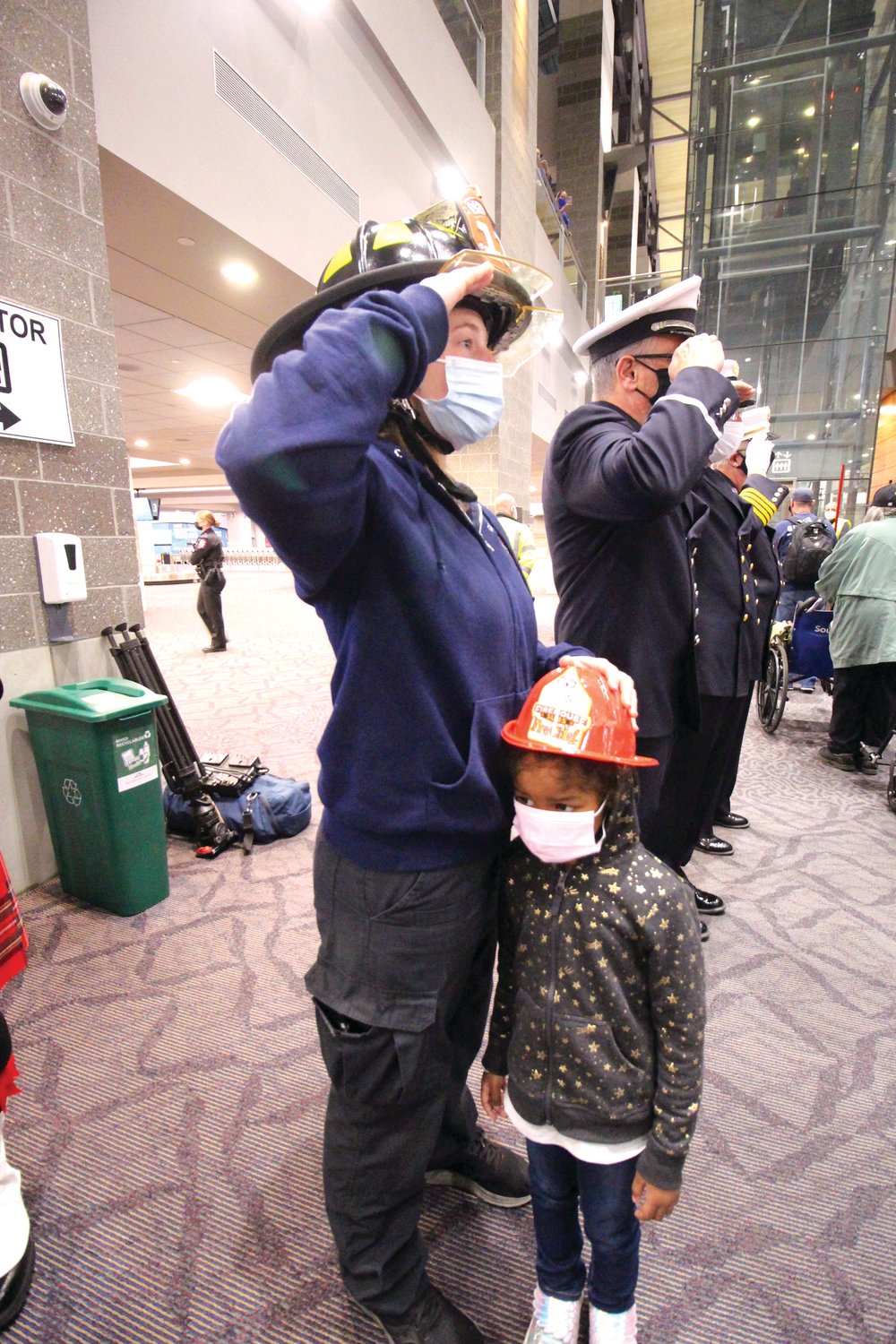 SALUTING THEIR SERVICE: Cranston firefighter recruit Jesse Ossian, her daughter Jaidyn at her side, welcomes veterans as they arrive at the terminal.
