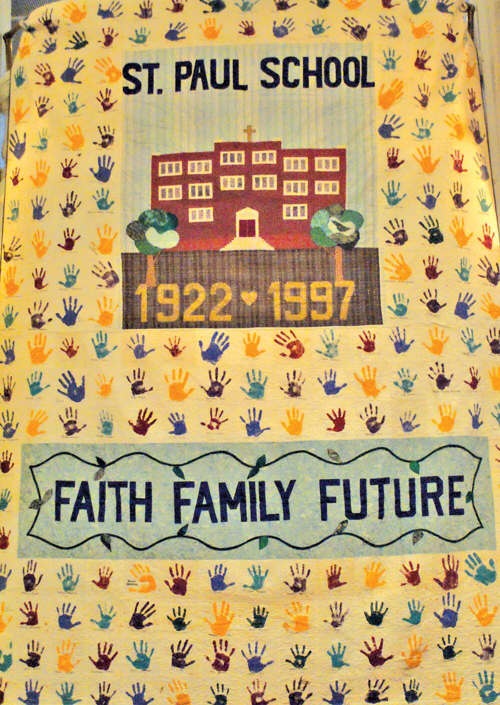 WOVEN FROM HISTORY: This quilt was made for St Paul School’s 75 anniversary by Gail Kelleher. Each handprint on the quilt is an actual handprint from every student and faculty member that attended the school in 1997. One space was left empty to represent every student to attend before that year and all those who would attend after. (Photo by Steve Popiel)